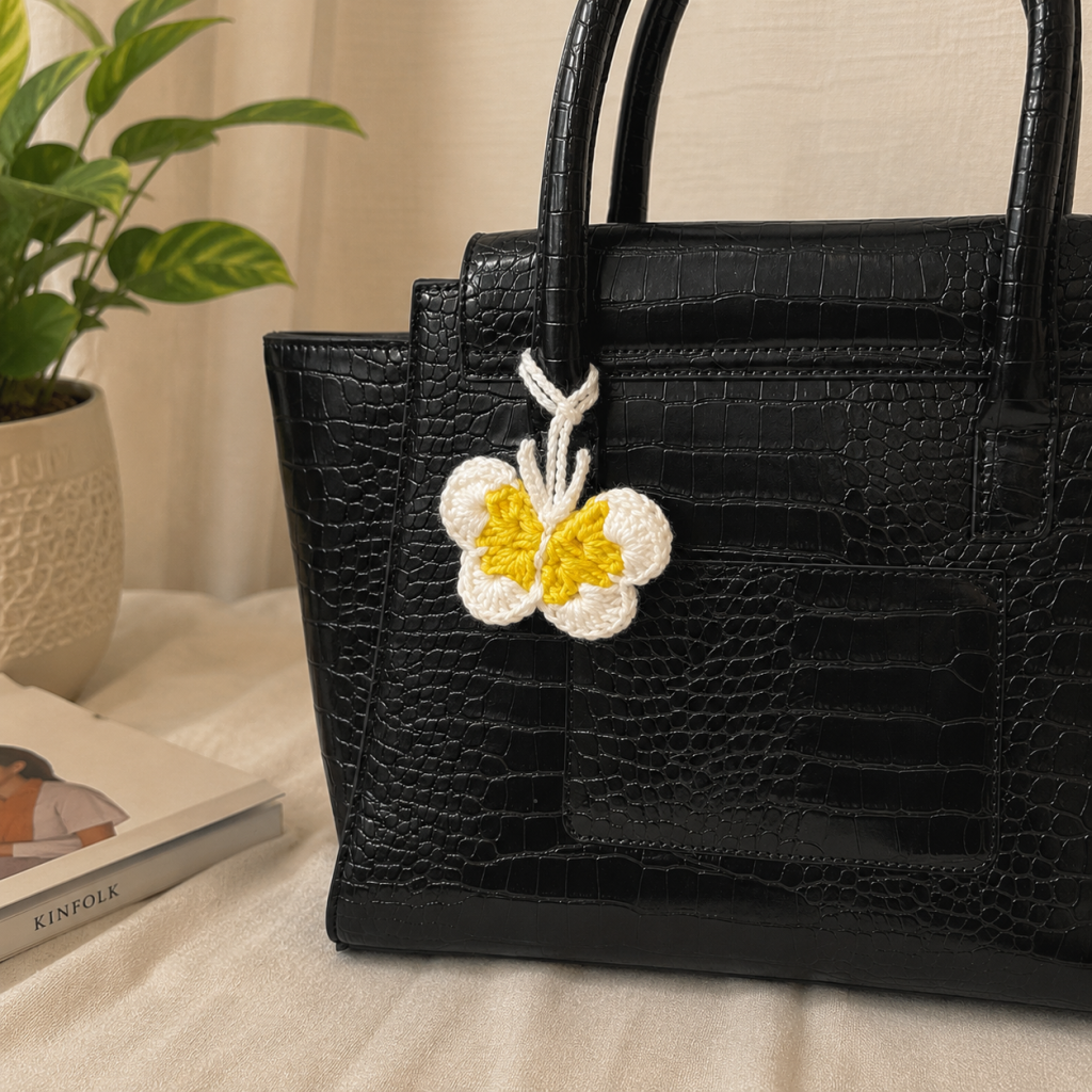 Crochet butterfly bag charm in lwhite and yellow attached to a black handbag