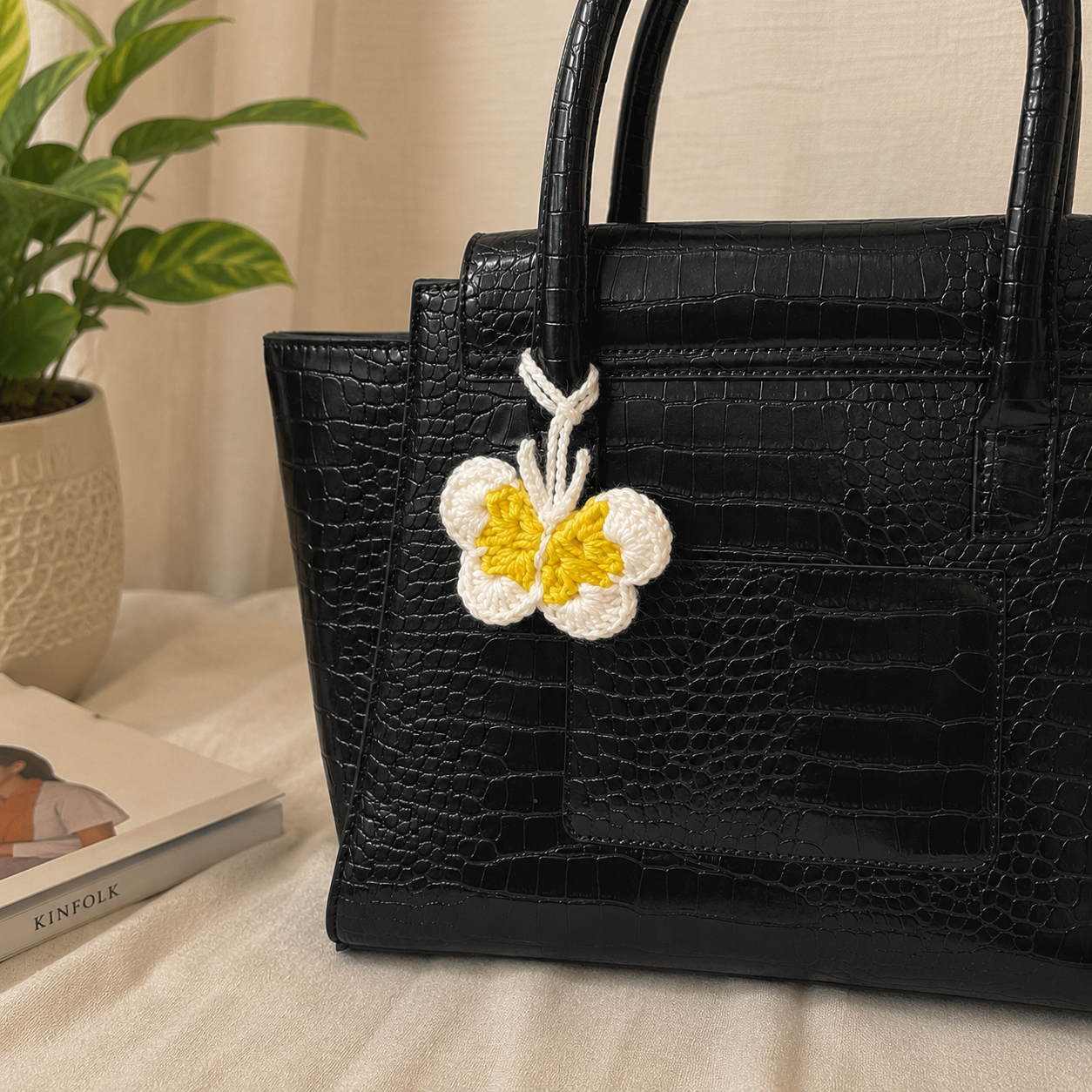 Crochet butterfly bag charm in lwhite and yellow attached to a black handbag
