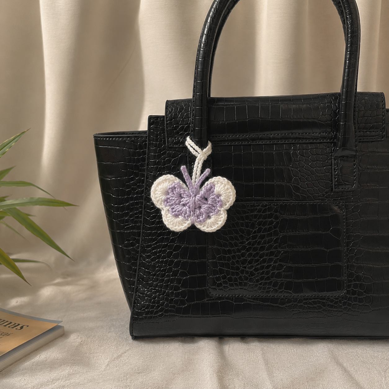 Crochet butterfly bag charm in lavender and white attached to a black handbag
