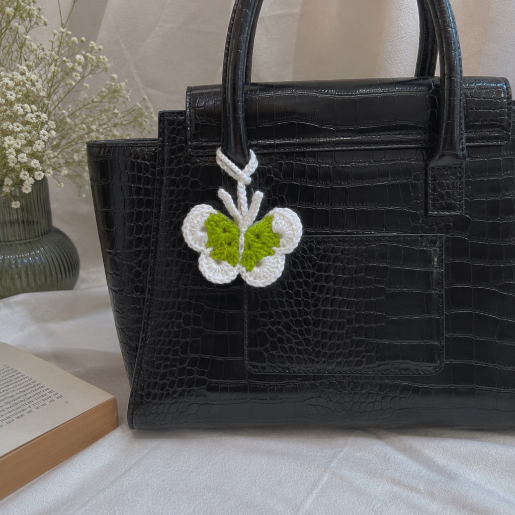 Crochet butterfly bag charm in green and white attached to a black handbag
