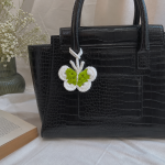 Crochet butterfly bag charm in green and white attached to a black handbag